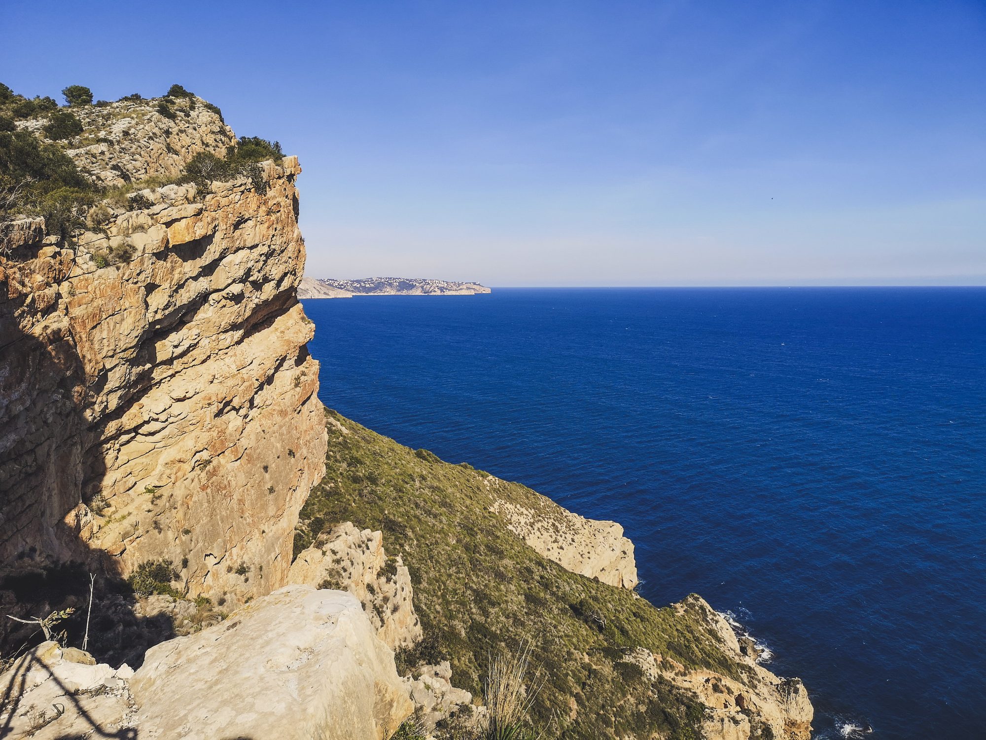 Golden sea cliffs of Cap d'Or above deep blue water, Moraira