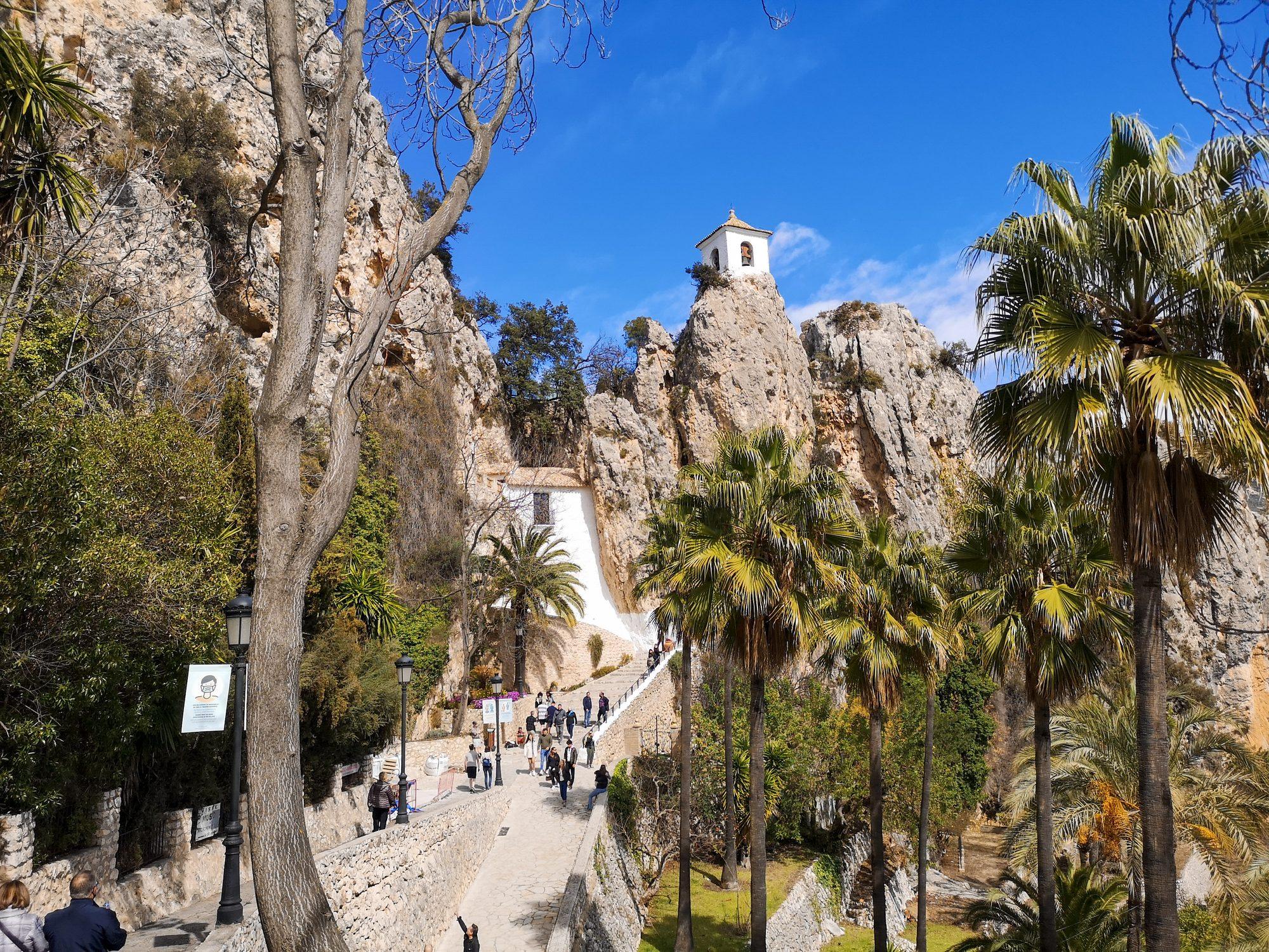 Path lined with palms leading up to the bell tower on its rock, Guadalest