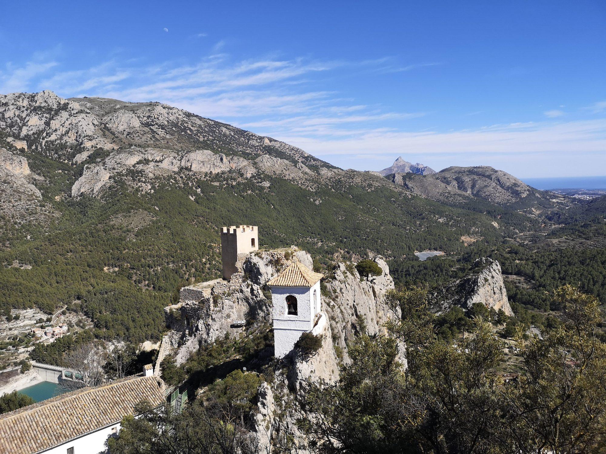 Free-standing bell tower and stone tower of Guadalest seen from above, with the mountains and the sea